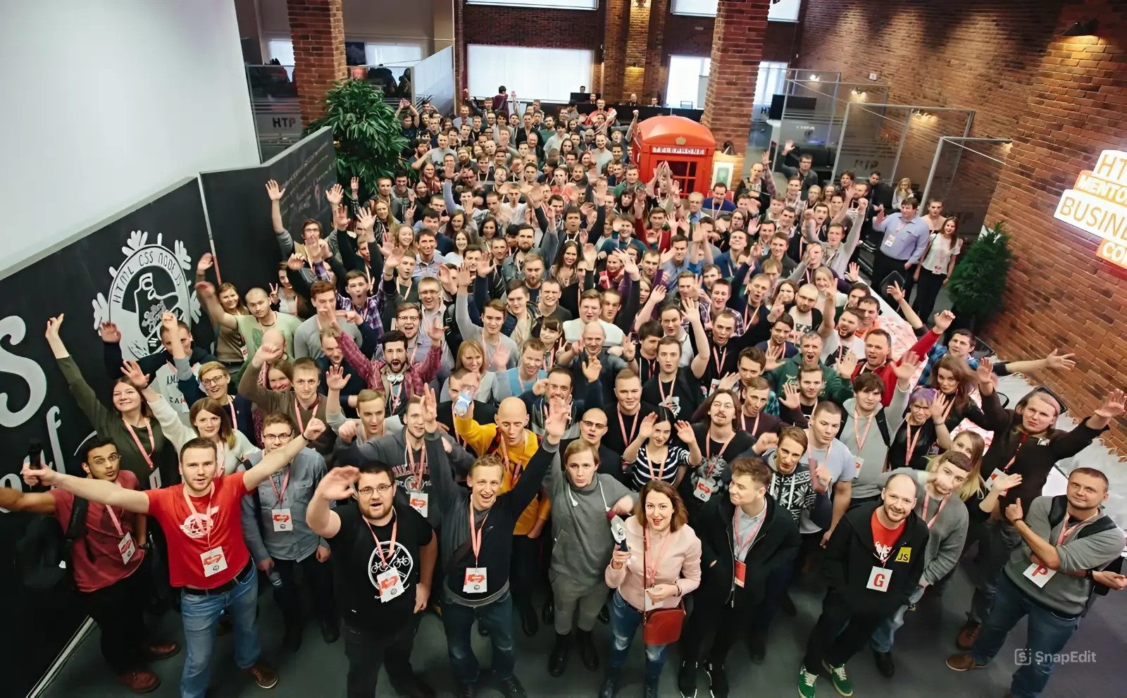 Group of conference attendees indoors, smiling and waving at the camera with name tags